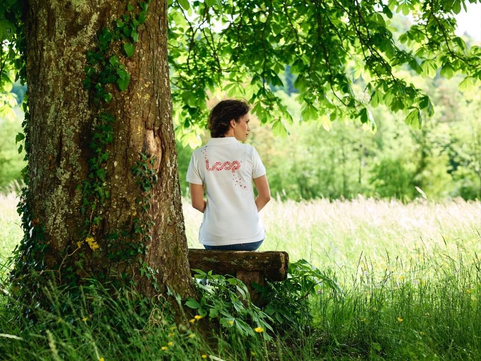 Eine Frau sitzt draussen unter einem Baum und trägt ein weisses Shrit mit einem Loop Logo, das von Pandinavia stammt.