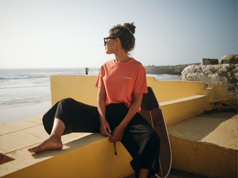 Frau mit einem NIKN Shirt mit dreamer Embroidery sitzt still am Meer und blick in die Weite.