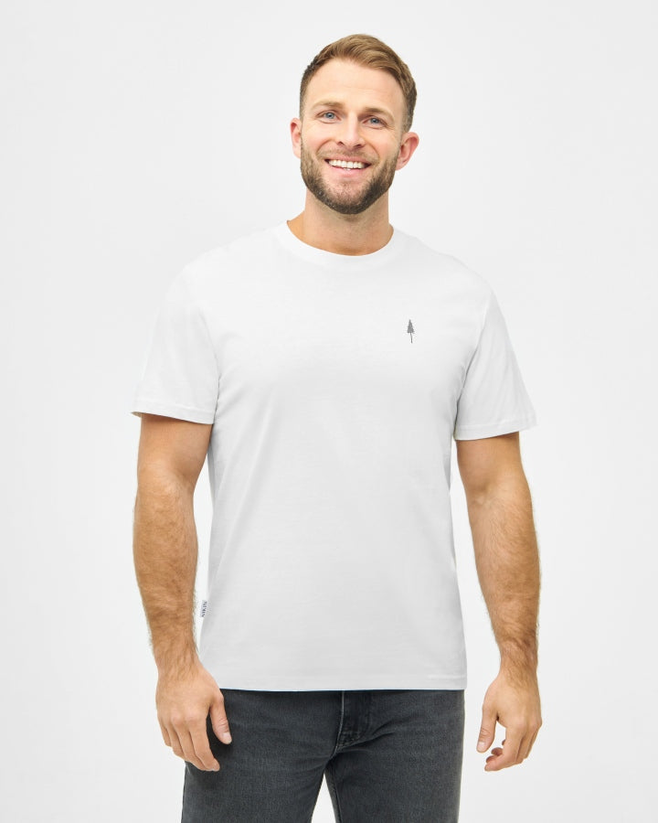 NIKIN TreeShirt White Herrenshirt Baumwolle, kombiniert mit dunklen Jeans, vor hellgrauem Hintergrund.