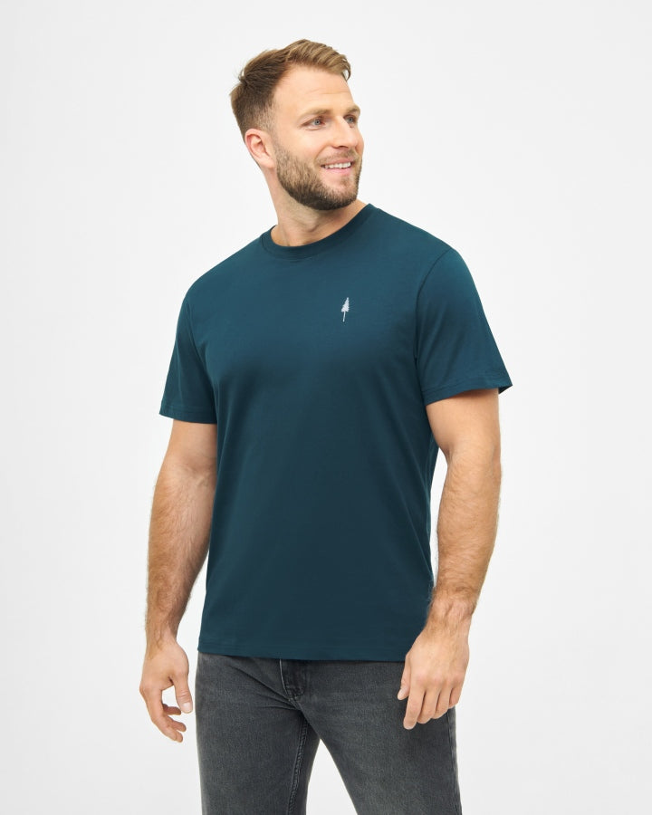 NIKIN TreeShirt Herren T-Shirt, teal, kleines Logo, Modell stehend und lächelnd, leicht seitlich gedreht.