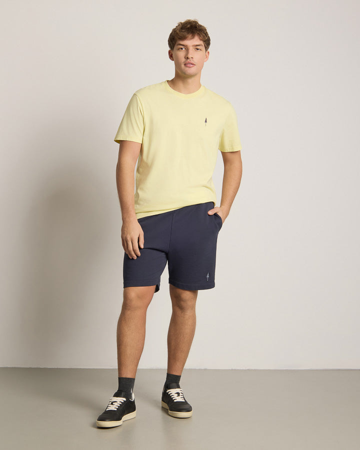 NIKIN TreeShirt Herren T-Shirt gelb, kombiniert mit navy Shorts und Sneakers, vor heller Wand.