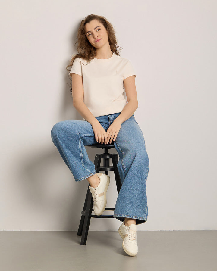 NIKIN TreeShirt Women Porcelain Damen T-Shirt, lange lockige Haare, neutraler Hintergrund, präsentiert auf Hocker.