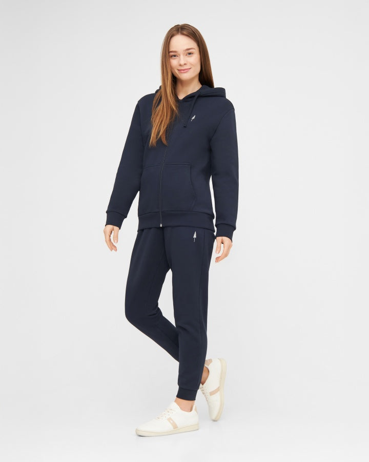 NIKIN Veste TreeHoodie pour femme, bleu foncé, avec un pantalon de jogging et des baskets blanches sur fond clair.