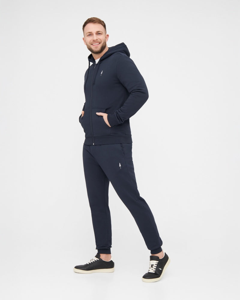 NIKIN TreeHoodie-Kapuzenjacke für Herren, dunkelblau, kombiniert mit einer Jogginghose und schwarzen Sneakern, vor weißem Hintergrund.