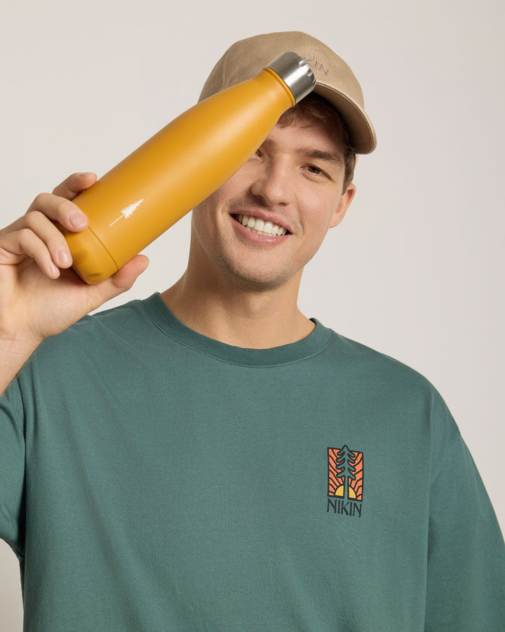 NIKIN TreeBottle „Mustard Glas“, gehalten von einer Person mit grünem Shirt und beiger Mütze, Produktfoto Schweiz.
