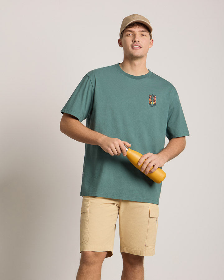 NIKIN Gourde TreeBottle « Mustard », jaune, tenue par un mannequin vêtu d'un t-shirt vert devant un fond neutre.