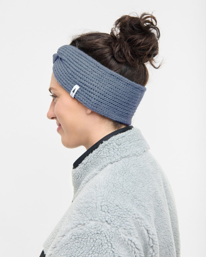NIKIN TreeHeadband Bandeau torsadé en tricot, blau, en plastique, femme au profil avec des fesses et une veste en laine polaire plus épaisse.
