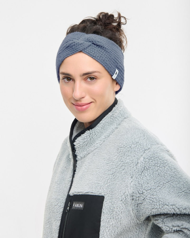 NIKIN TreeHeadband Strick-Twist Stirnband, cosy, Farbe Steel Blue, getragen von Frau mit grauer Fleecejacke vor Weiß.