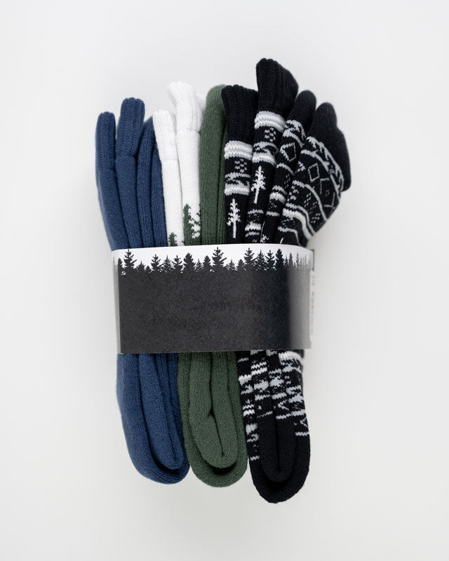 The Essential Kit TreeSocks Bundle features five pairs of socks in blue, white, green, and black—some with Nordic patterns. The set is wrapped in a black and white paper band with a forest silhouette.