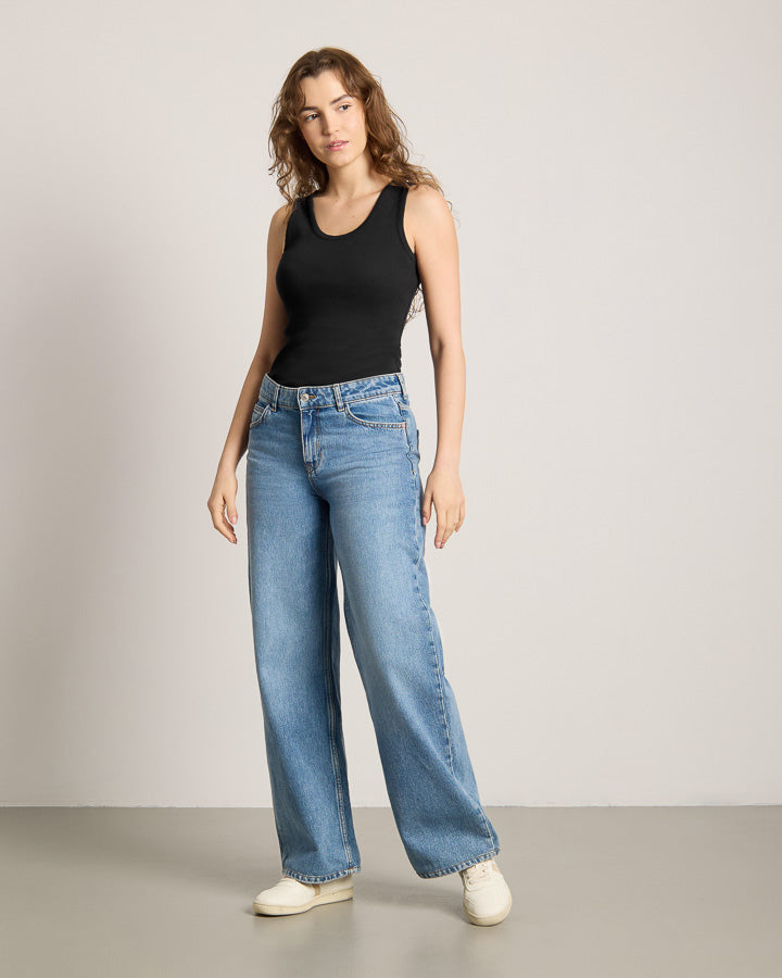 NIKIN TreeTop Women Black Top Damen, weiter Schnitt, kombiniert mit blauen Wide-Leg Jeans und weissen Schuhen.