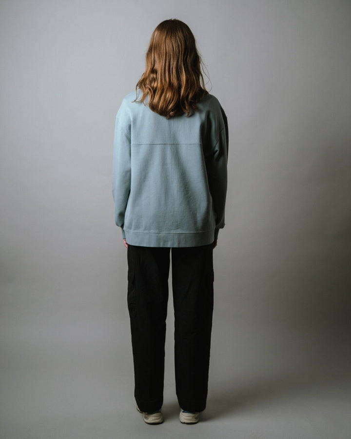 NIKIN  TreeSweater Quarter Zip Muntogna Elemental Blue Pullover, schwarz Hose, Person von hinten, lange Haare.