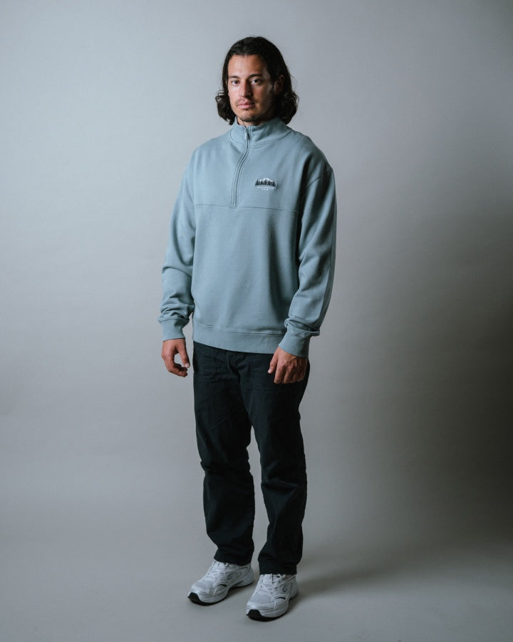NIKIN  TreeSweater Quarter Zip Muntogna Elemental Blue Herrenpullover, Farbe Blau, kombiniert mit schwarzen Hosen.