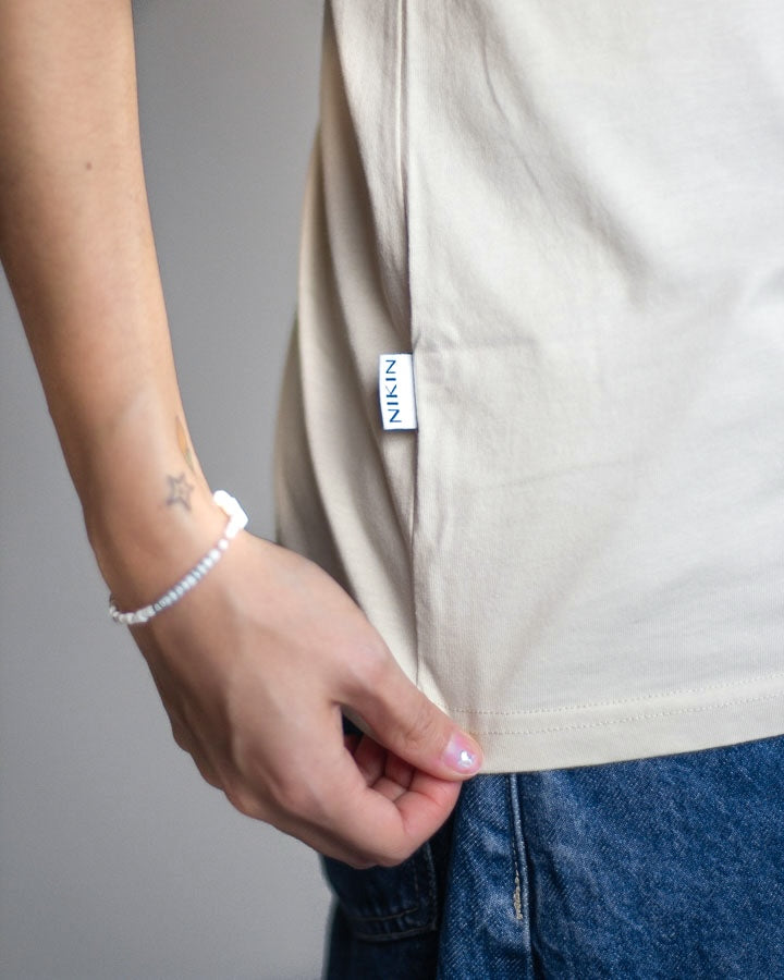 NIKIN TreeShirt-Jubiläums-T-Shirt „Relaxed Pumice“, Rückendruck „Treehugger“, blaue Jeans, sichtbares Tattoo.