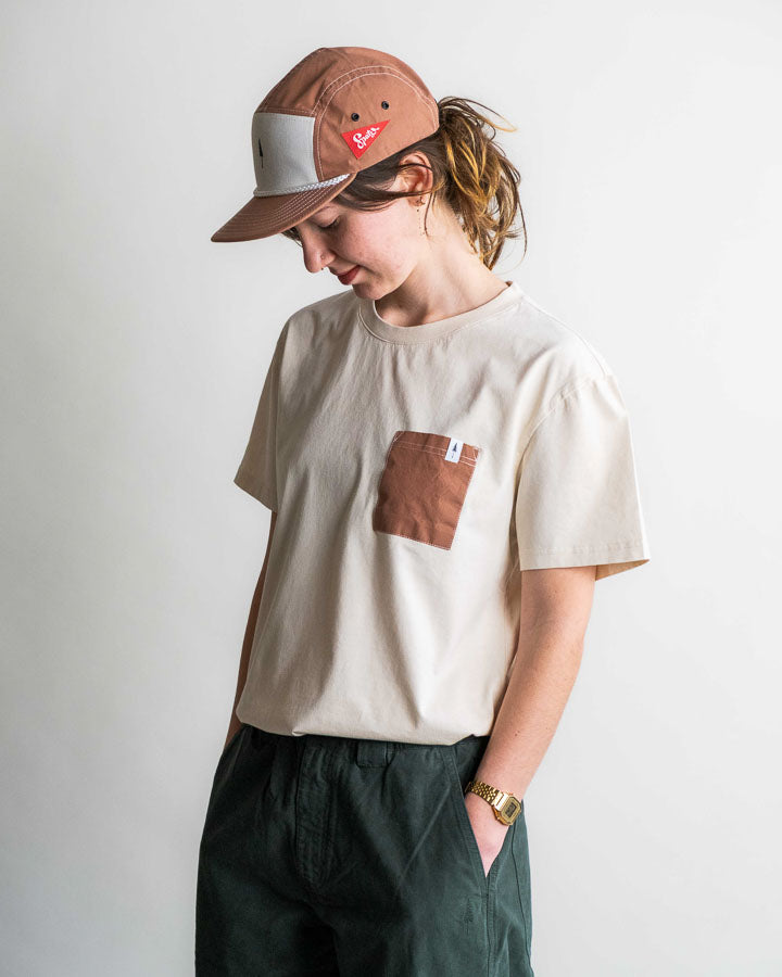 NIKIN TreeShirt Pocket Spatz Chalk T-Shirt, Unisex, dunkel, mit Brusttasche, kombiniert mit einer dunklen Hose und einer braunen Mütze.