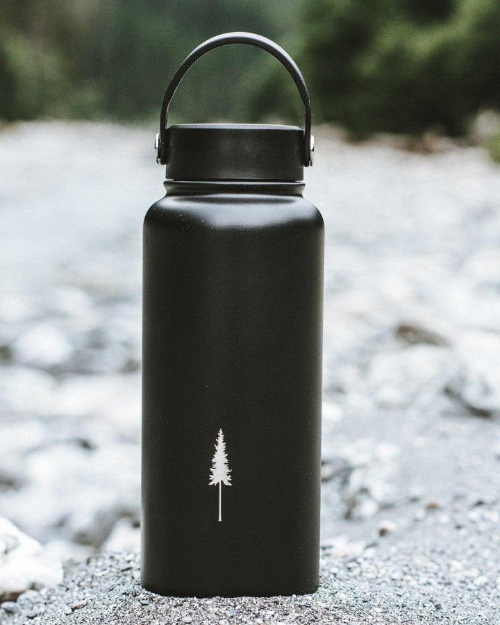 NIKIN TreeBottle Outdoor 1 l Trinkflasche, schwarz, Baumlogo, Farbe: Schwarz, auf Felsen am Flussufer.